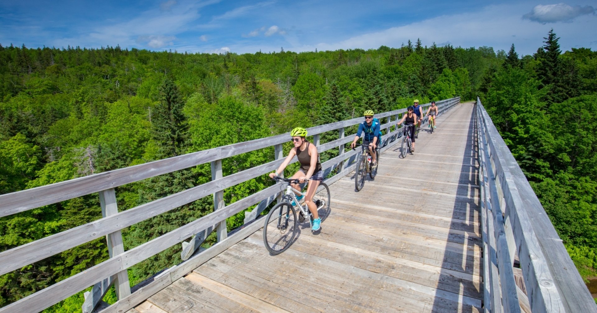 five riders bike along a long wooden bridge